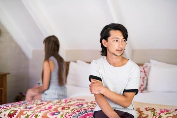 Sad young man with woman ignoring on bed