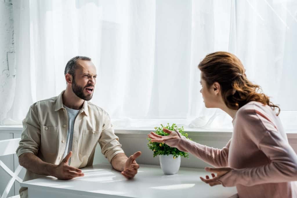Selective focus of angry man gesturing and looking at woman while sitting at home