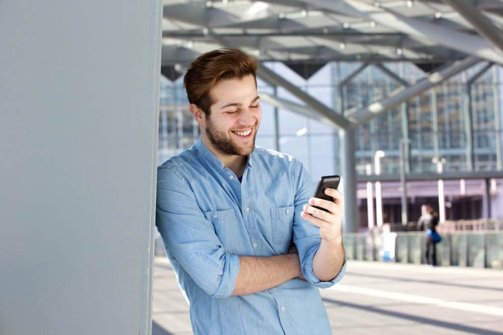 Close up portrait of a smiling man reading text message on mobile phone