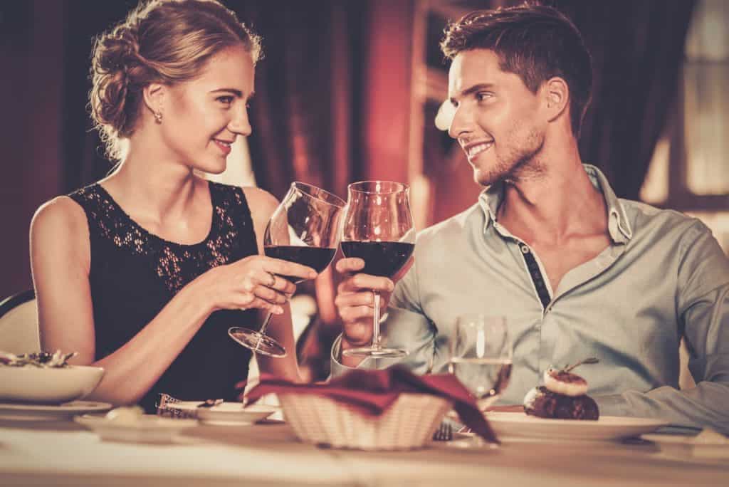 Beautiful young couple with glasses of red wine in luxury restaurant