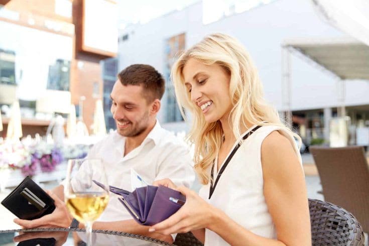 happy couple with wallet and wine glasses paying bill at restaurant