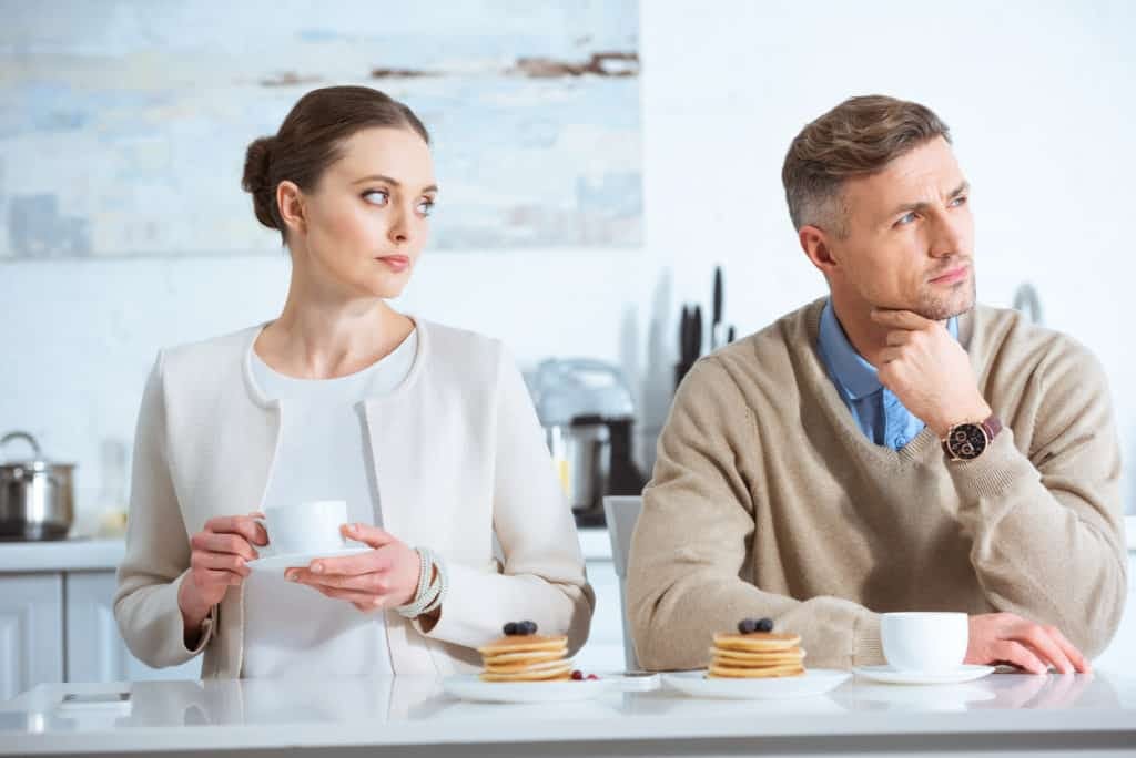 Selective focus of adult man ignoring sad woman during breakfast in morning