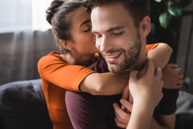Tender woman embracing happy boyfriend and whispering in his ear