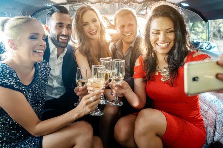Party people in a limo with drinks taking a selfie with phone smiling into the camera