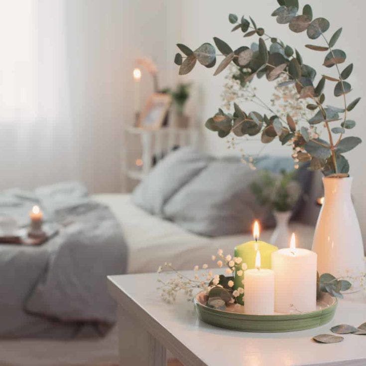 burning candles and eucalyptus in vase in white bedroom