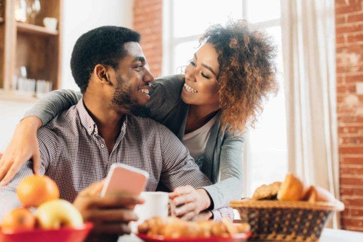 Loving young couple using smartphone in kitchen